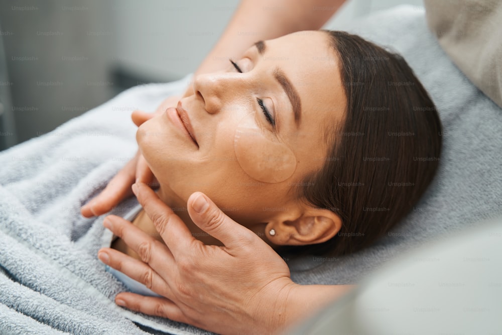Close up portrait of a pleased young woman having her neck massaged by a professional dermatologist