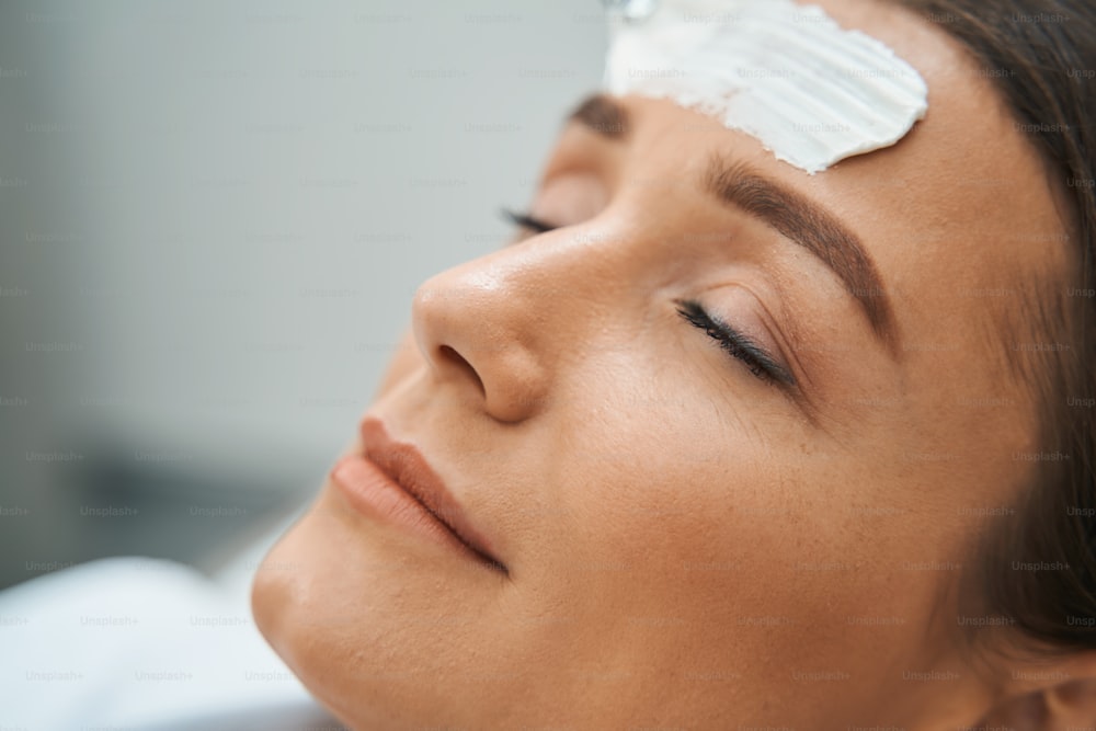 Ritratto ravvicinato di una serena cliente della spa con gli occhi chiusi che sonnecchia durante una procedura cosmetica