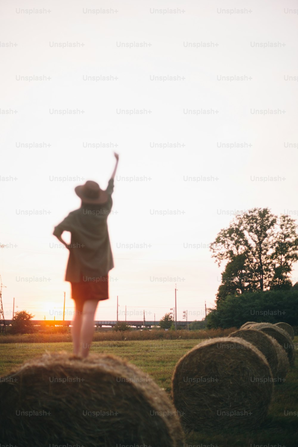 Blurred silhouette of happy woman on haystack enjoying evening  and focus on going train in sunset summer field. Young happy female relaxing on hay bale in countryside. Atmospheric  moment