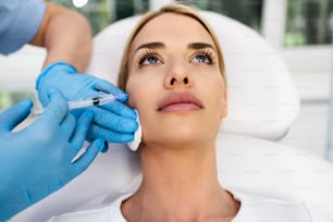 Una atractiva mujer rubia está recibiendo inyecciones faciales rejuvenecedoras en una clínica de belleza. La experta esteticista está rellenando las arrugas femeninas con botulinum.