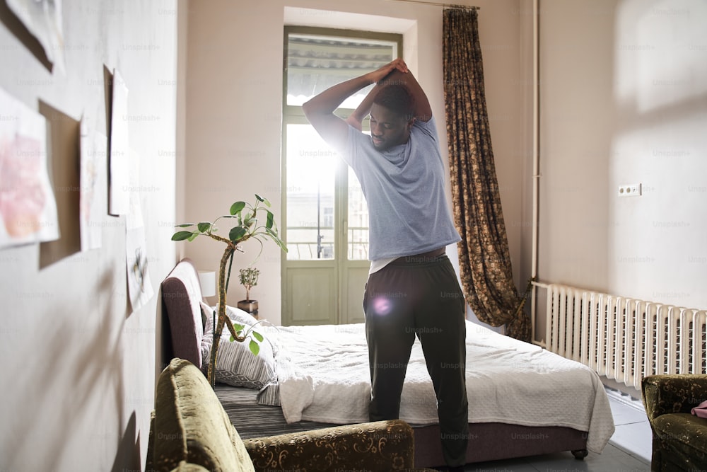 Stretching. Full length view of the multiracial man stretching his arms while doing his morning exercises at home. Sport and recreation concept. Stock photo