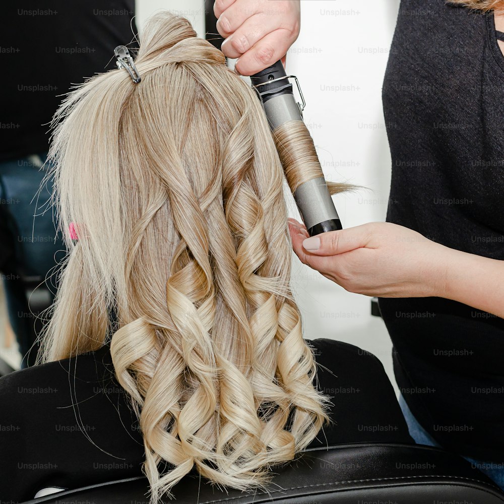 Stylist making a hairdo with hair curler for blond woman after hair dyeing.