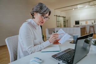 Retrato de una mujer madura aprendiendo un idioma extranjero usando una computadora portátil en casa. Educación en línea utilizando el concepto de tecnología. Concepto de distancia social. Enfoque selectivo.