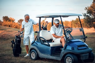 コートに立つ2人のシニア男性ゴルファー。ゴルフカートに座っている男。