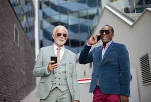 Two business men outdoors. Using smart phones.