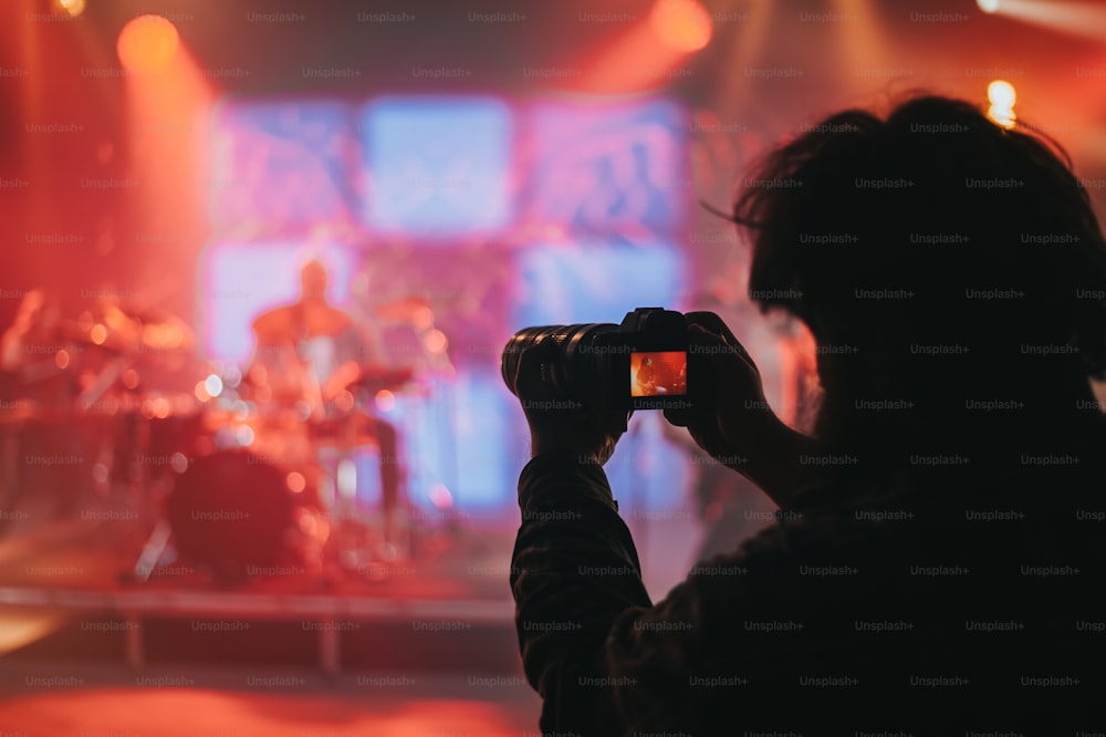 フェスティバルのコンサート中にピンクのライトでステージ上のミュージシャンを撮影する写真家のシルエット