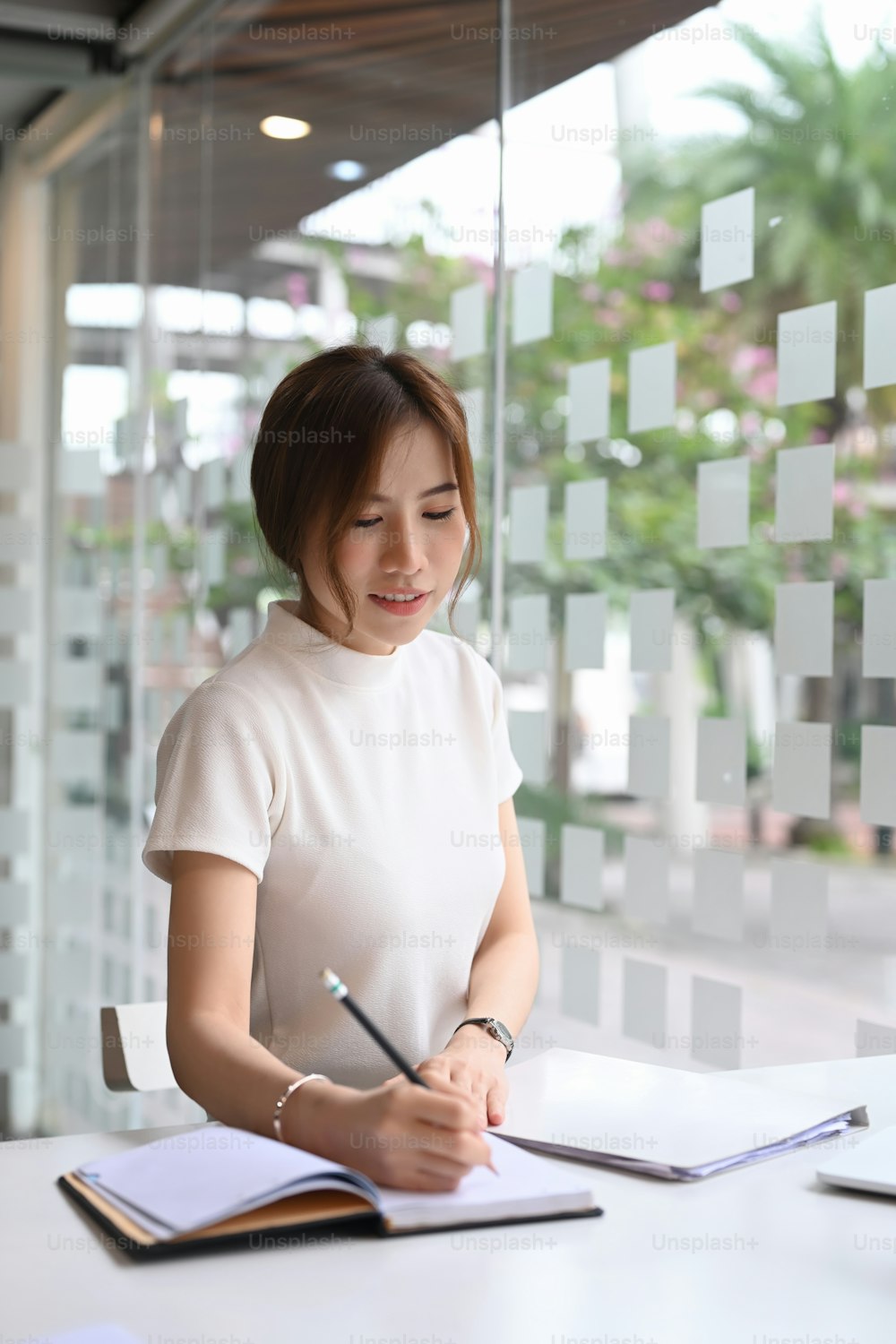 Woman writing notebook with pen on office workspace.