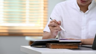 Empresário recortado escrevendo caderno com caneta sobre mesa em home office.