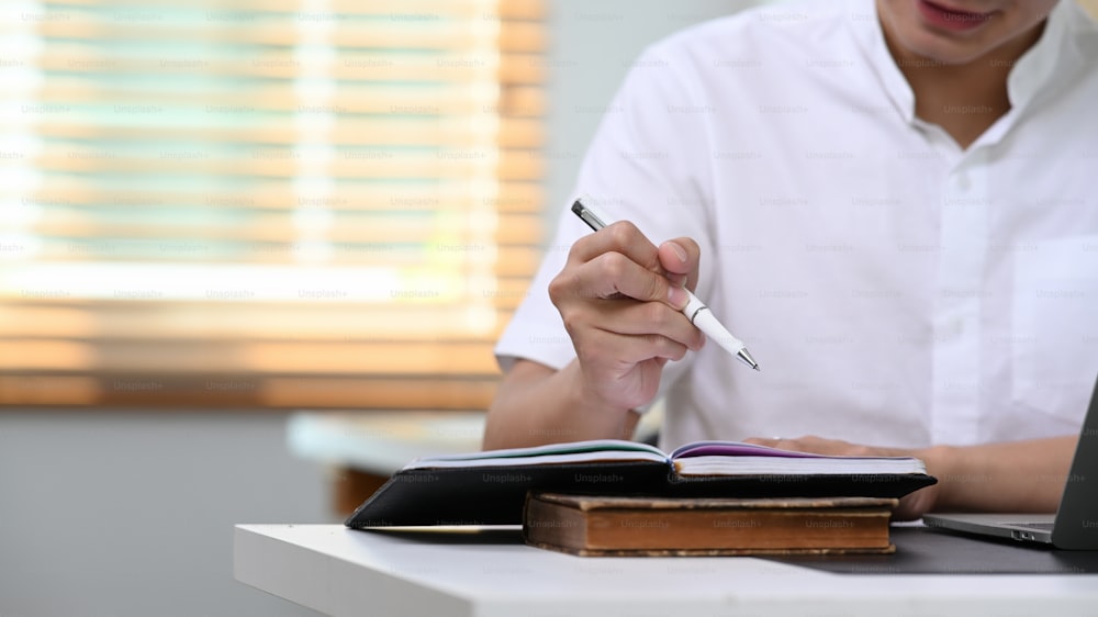 Cropped shot businessman writing notebook with pen on table at home office.