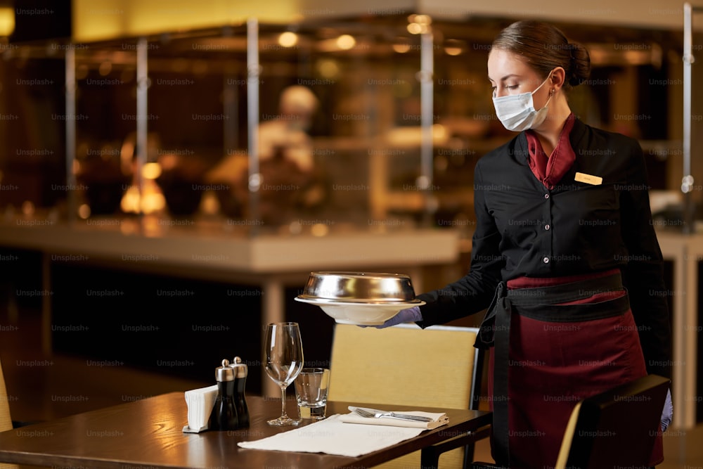 Copy-space photo of a professional waitress using protective mask while serving food to the tables in restaurant