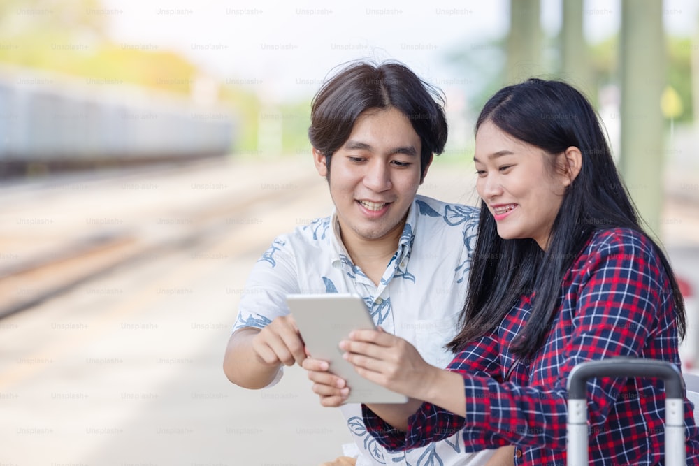 若いアジアのカップルのバックパッカーは、鉄道駅で目的地の旅行を見つけるためのタブレットを使用しています