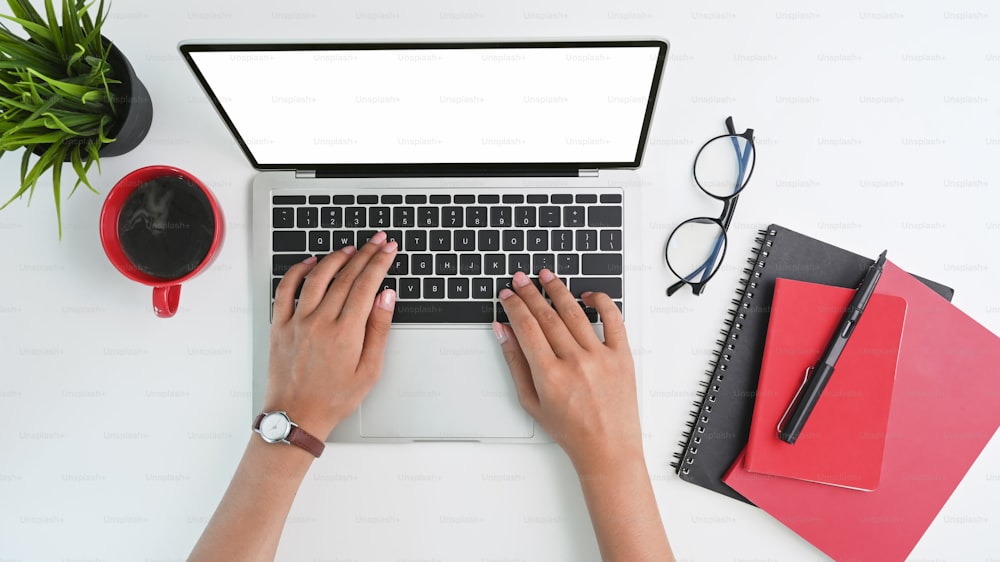 Mano de la mujer del espacio de trabajo de la vista superior escribiendo en la computadora portátil de la maqueta con la pantalla vacía y aislada.