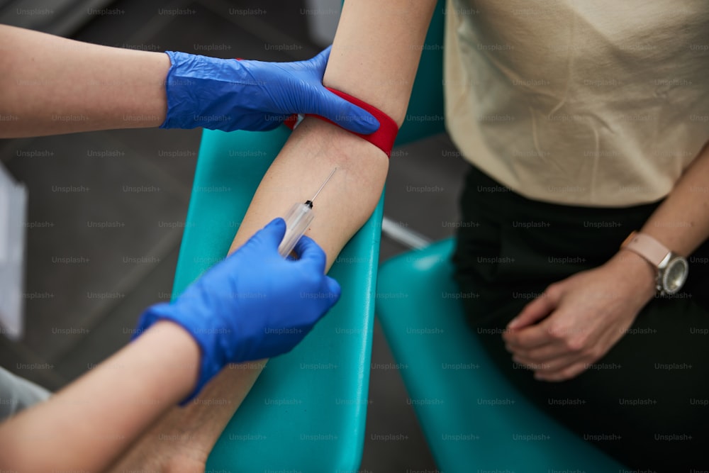 Foto recortada de una enfermera con guantes de látex insertando la aguja de la jeringa en el vaso del paciente