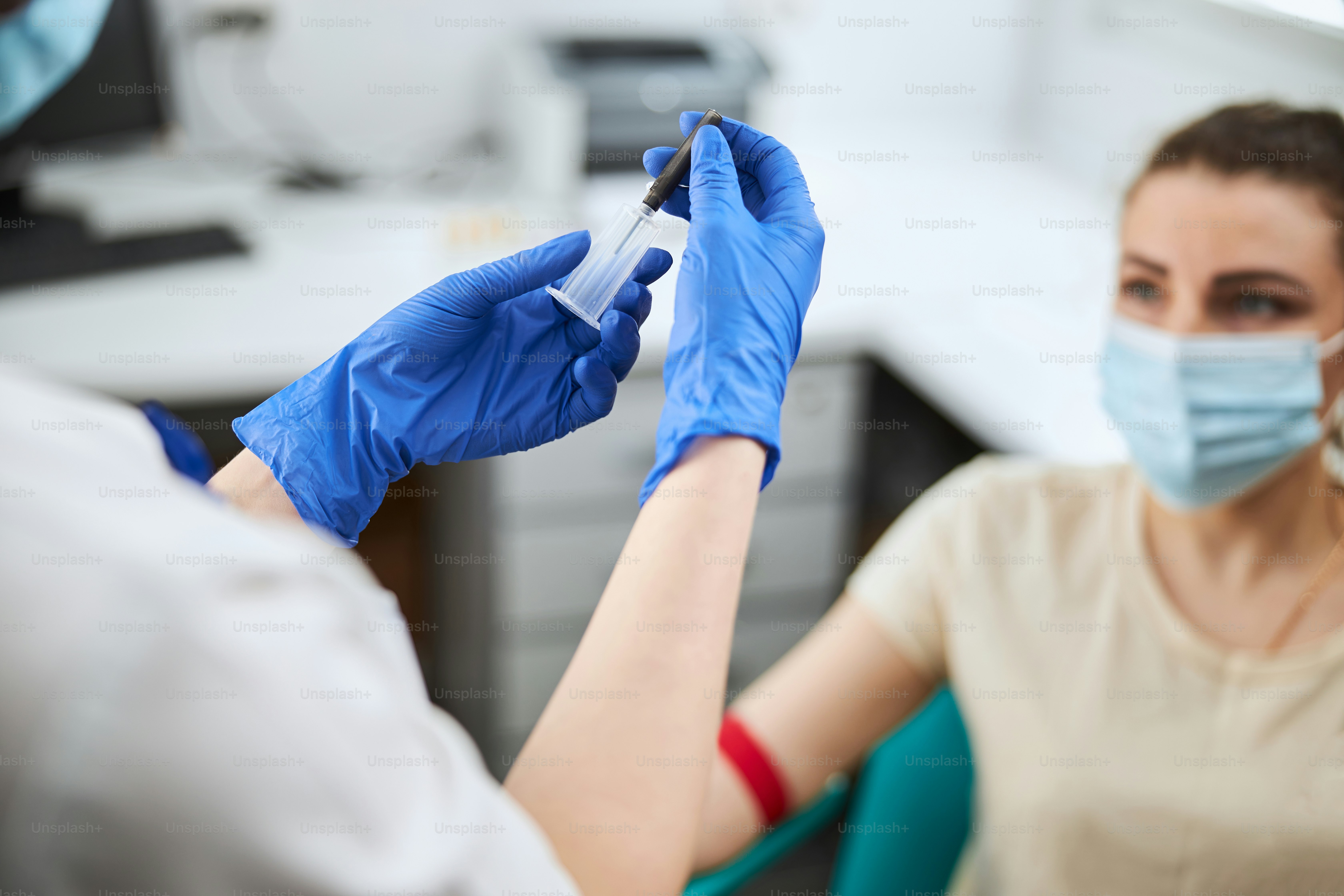 Experienced phlebotomy technician assembling the syringe in front of a young patient in a face mask