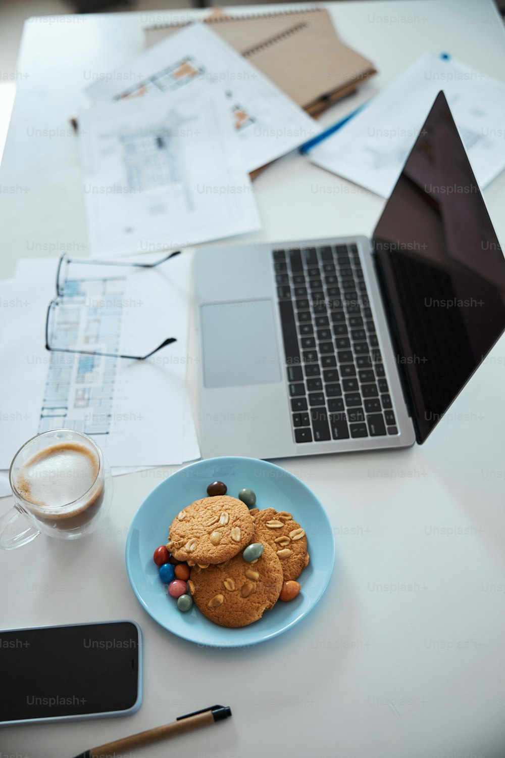 Workplace with notebook, cup of hot drink, architectural plans and plate of biscuits on office desk