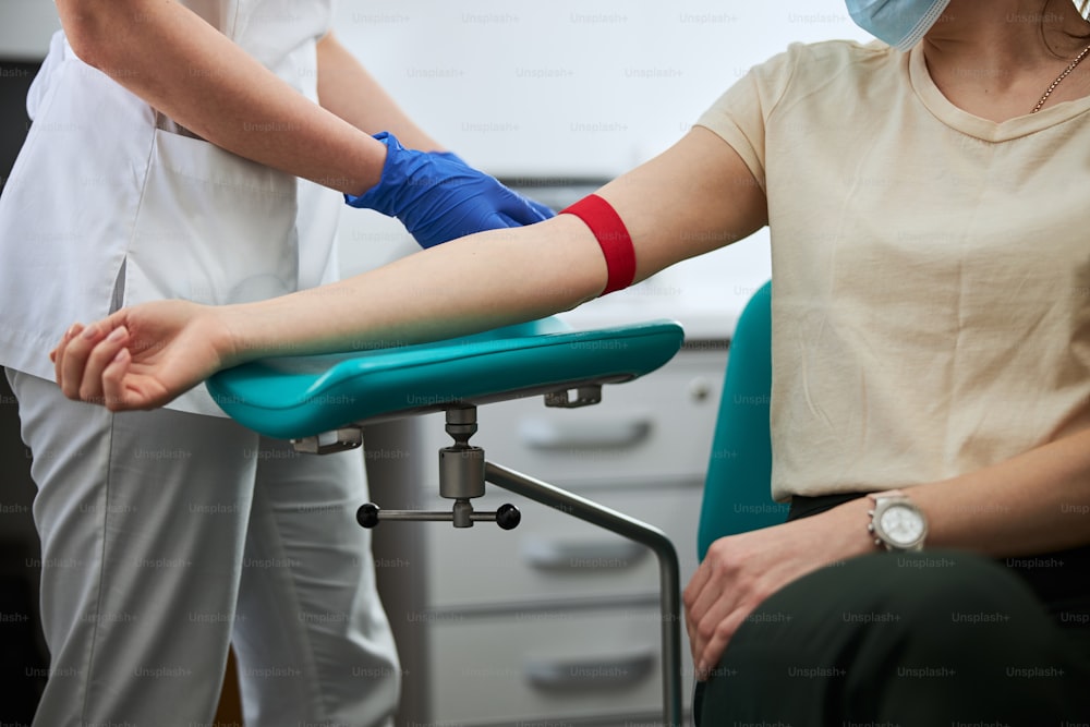 白人女性の瀉血専門医が、選択した穿刺部位の上に止血帯を装着している写真を切り抜いた写真