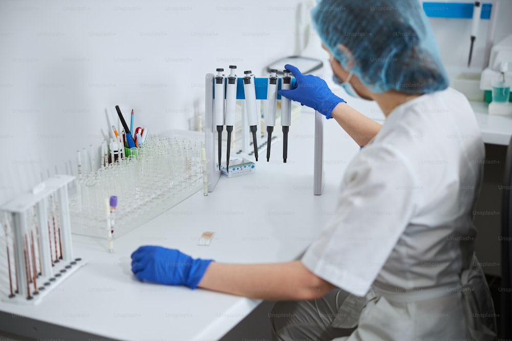 白衣と滅菌ラテックス手袋を身に着けた生化学者がテーブルに座っている後ろ姿
