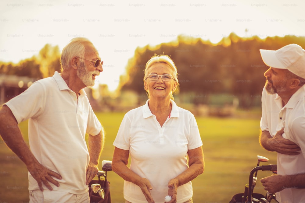 Drei lächelnde Seniorengolfer unterhalten sich auf dem Golfplatz.