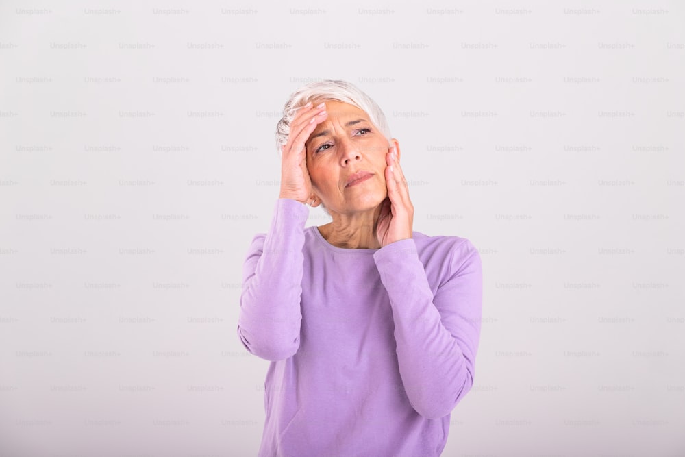 Mature woman holding her head with her hands while having a headache and feeling unwell. Senior woman with headache, pain face expression. Elderly woman having head pain migraine