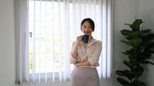 Confident young businesswoman holding coffee cup and smiling to camera.