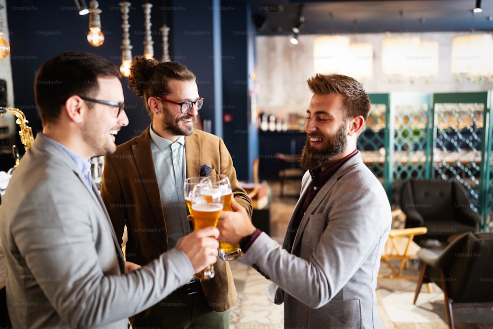 Happy business people drink beer after work in pub. Businessmen enjoy a beer.