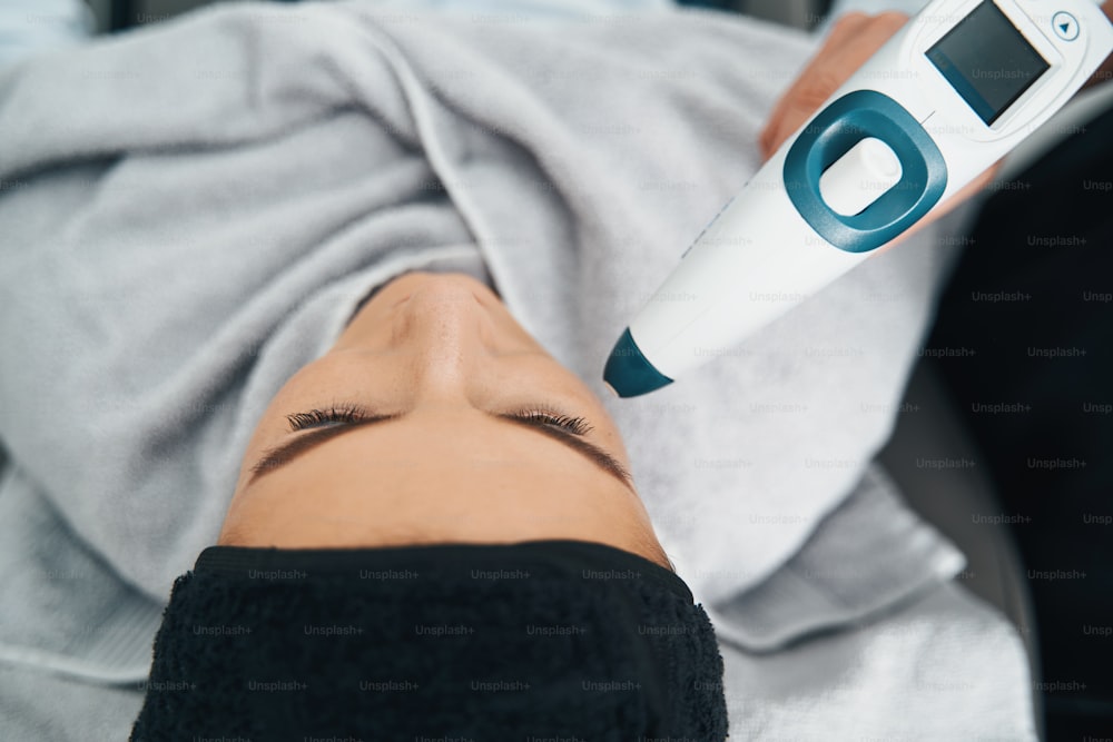 Top view of a Caucasian female patient undergoing a face-lifting procedure performed with a CO2 mesotherapy gun