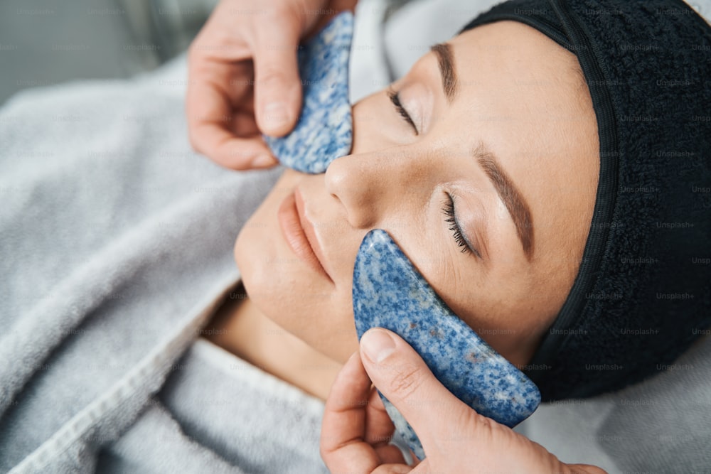Young woman facial skin being massaged with a pair of natural blue spot jasper boards