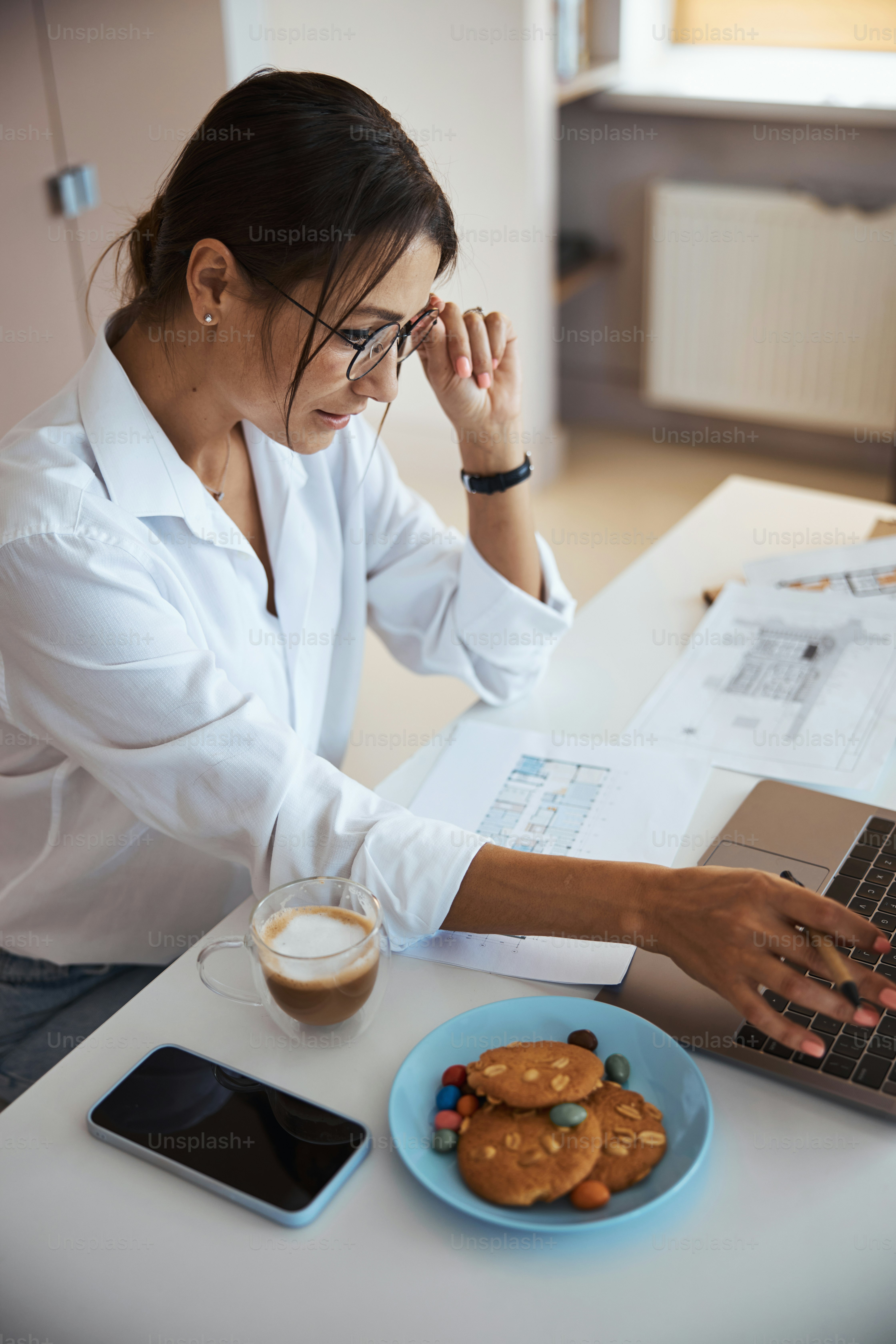 Beautiful businesswoman sitting at the table with papers and working on modern notebook in office
