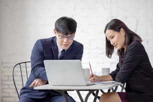 business man and woman sit at ther table looking at computer laptop