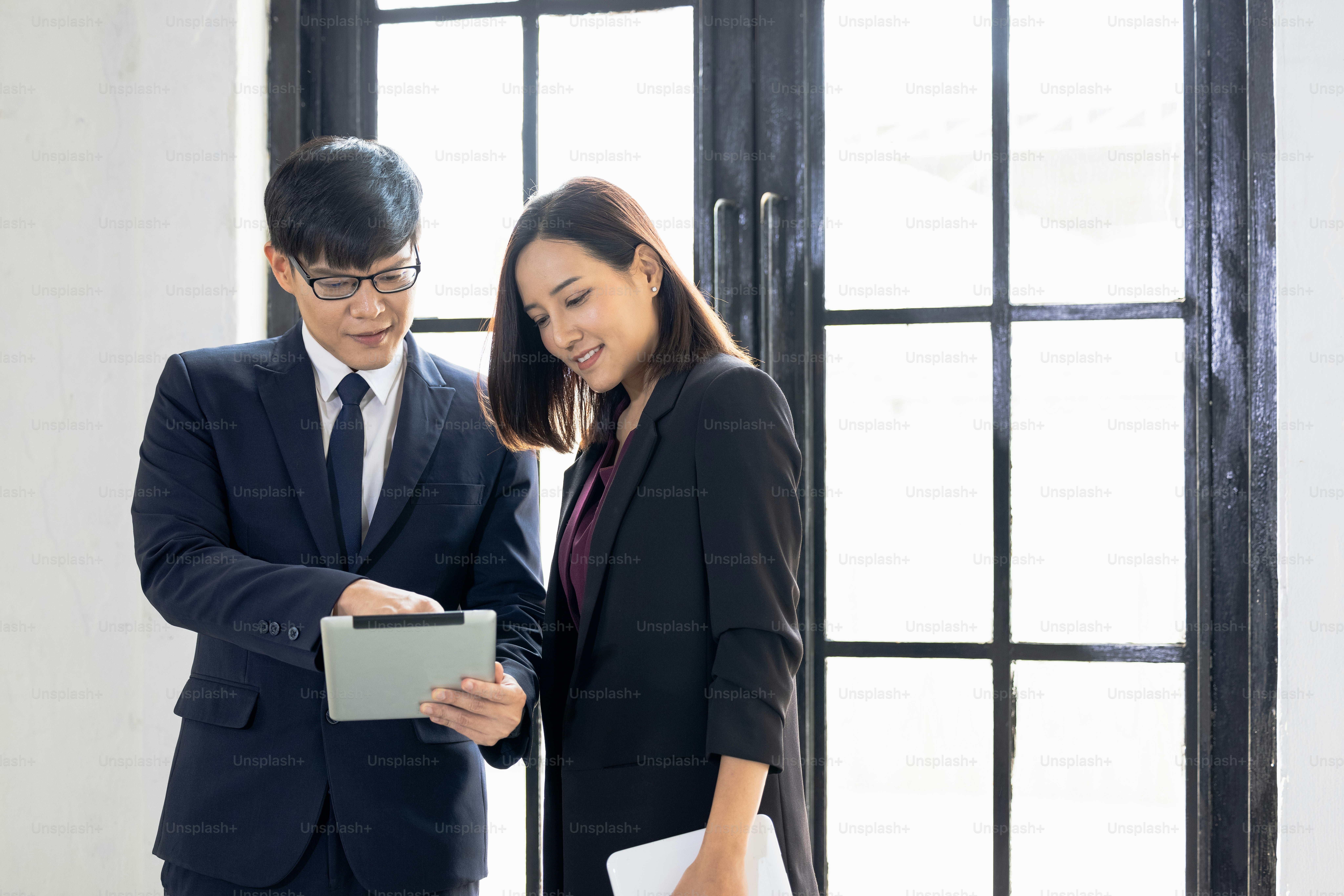 Businessman and businesswoman using a laptop together while standing near window in office