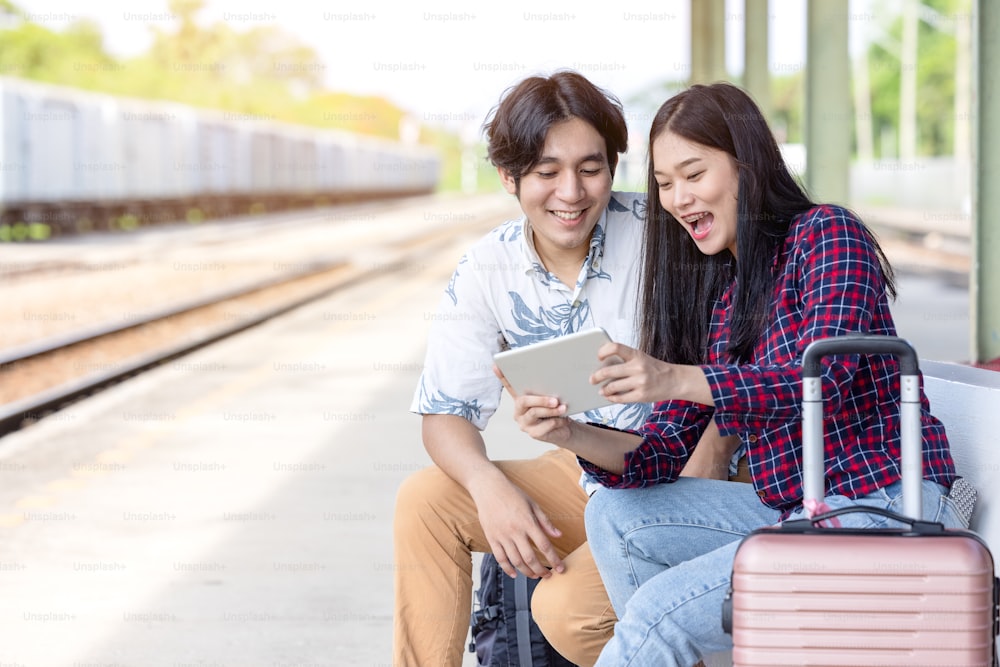 Joven mochilero de pareja asiática usando tableta para encontrar viaje de destino en la estación de tren