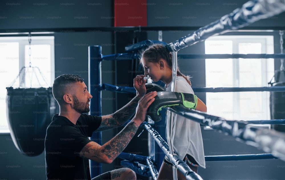 Concezione dell'assistenza. Giovane allenatore di boxe tatuato insegna a una bambina carina in palestra.