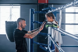 Concezione dell'assistenza. Giovane allenatore di boxe tatuato insegna a una bambina carina in palestra.