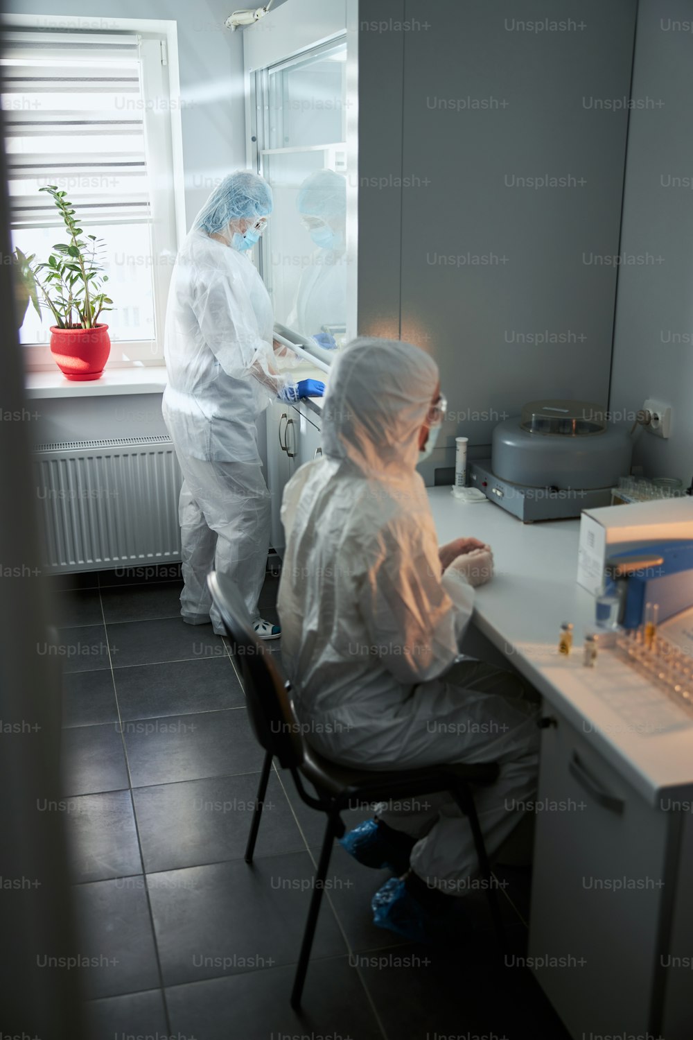 Two female colleagues in hazmat suits working with hazardous substances in a modern biosafety lab