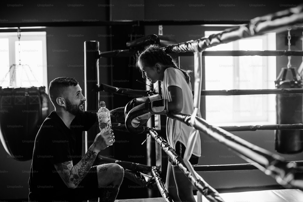 Concepção de assistência. Jovem treinador de boxe tatuado ensina garotinha fofa na academia.