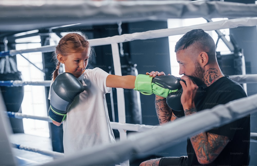 Avere sparring l'uno con l'altro sul ring di boxe. Giovane allenatore di boxe tatuato insegna a una bambina carina in palestra.