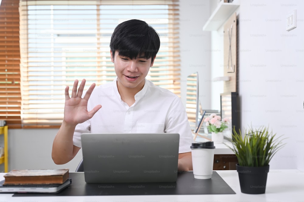 Young asian man sitting in modern office and video conference with his colleagues on laptop computer.