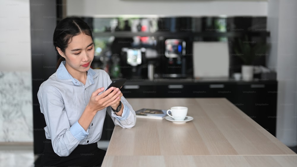 Giovane dipendente donna asiatica che utilizza il telefono cellulare durante la pausa caffè in ufficio.