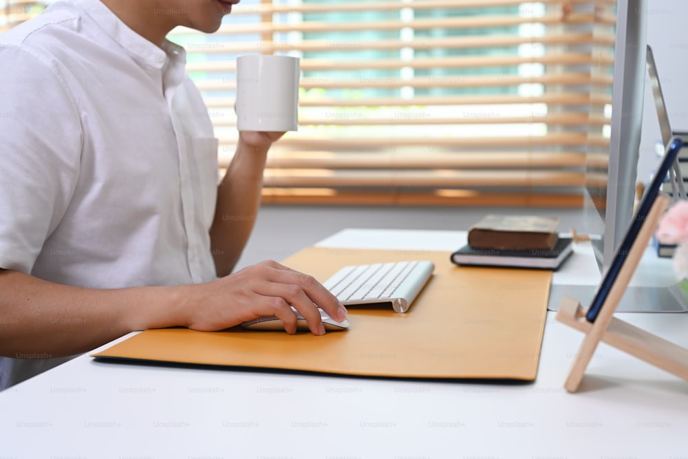 Cropped shot of young man holding coffee cup and working online at home office.