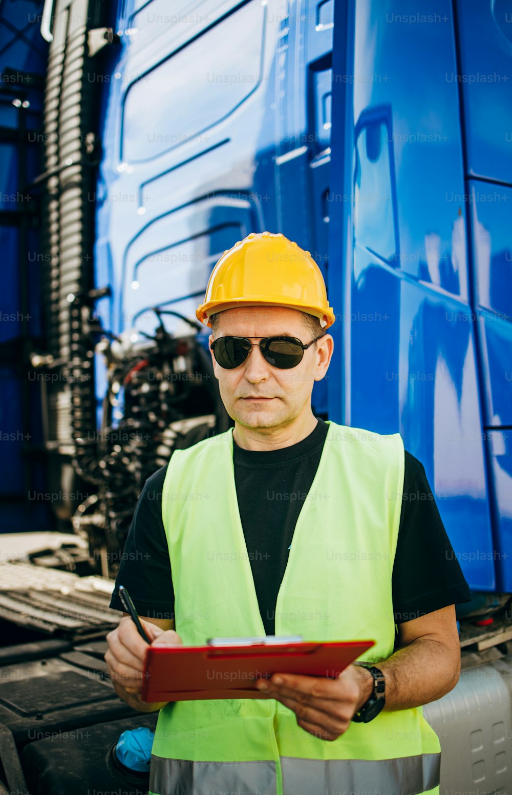 Professional male industrial truck driver with yellow protective helmet performs technical inspection of the vehicle as safety measures before next drive.