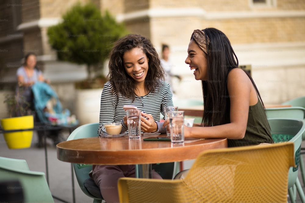 Dos mujeres en un café usando un teléfono inteligente.