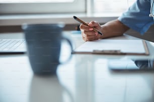 Primer plano de una trabajadora médica joven sentada en la mesa con una computadora portátil y completando el registro médico