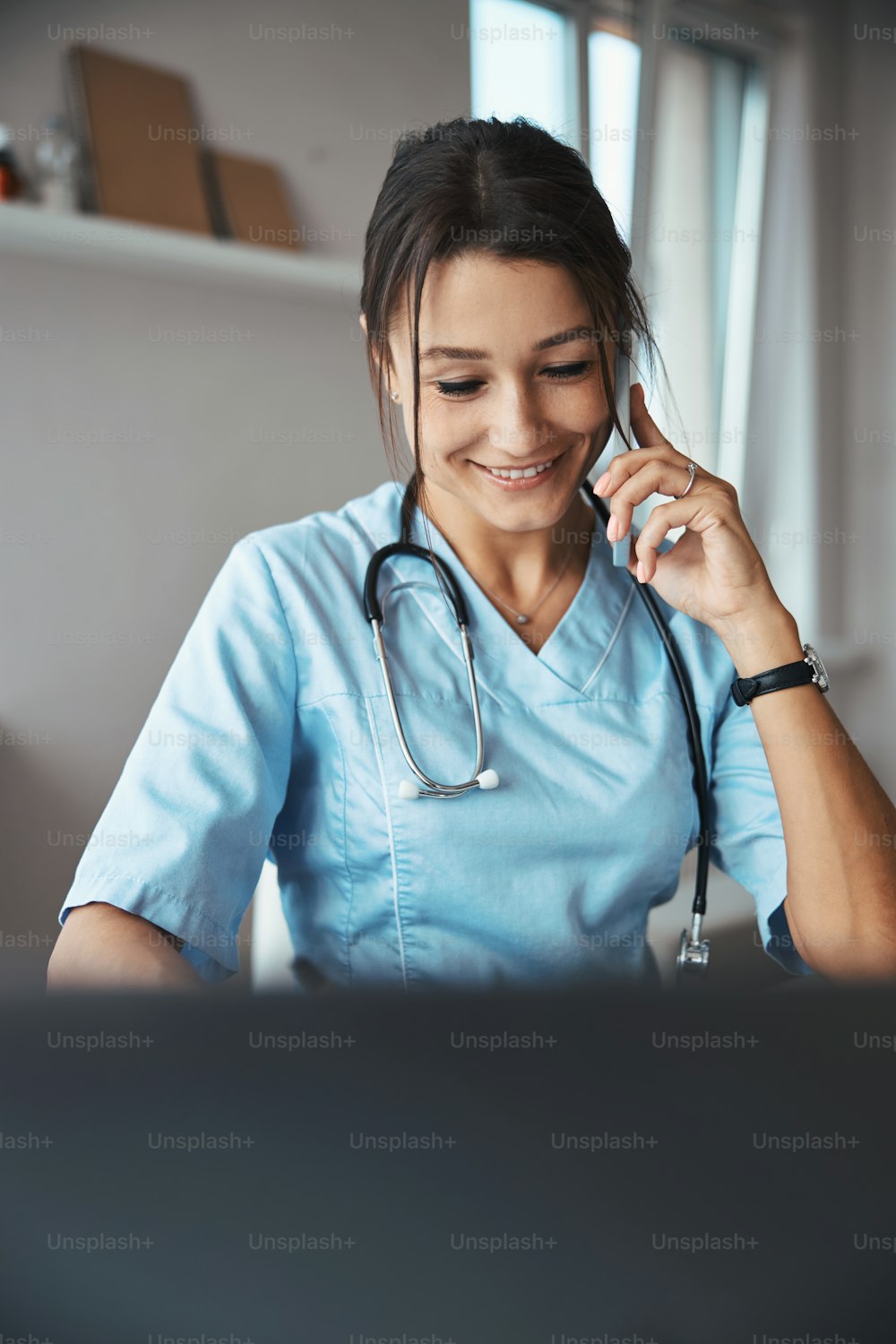 Schöne junge Ärztin, die auf dem Handy spricht und lächelt, während sie in der Klinik arbeitet