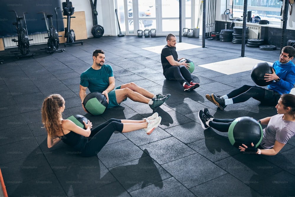 Grupo de cinco atletas caucásicos con pelotas de estabilidad sentados en el suelo durante el entrenamiento