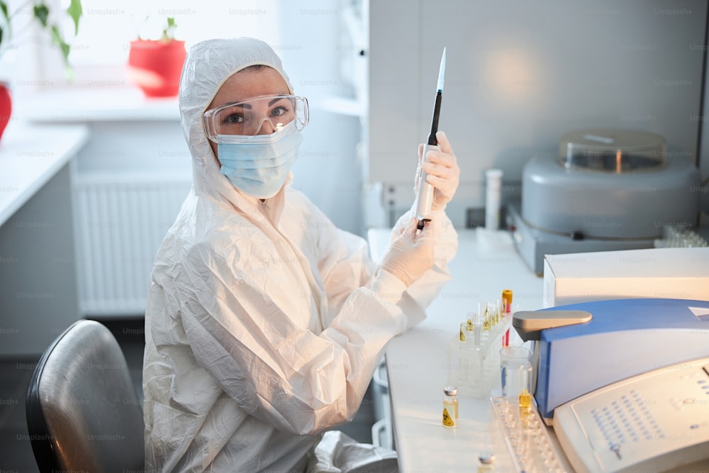 Female scientist in a hazmat suit and a mask holding the automated single-channel pipette in her hands