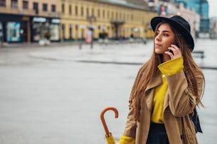 Giovane bella donna che usa uno smartphone e tiene un ombrello giallo mentre cammina in città in un giorno di pioggia