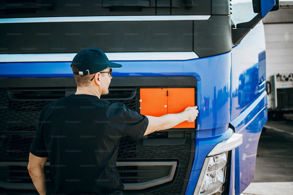 Professional truck driver with hat and sunglasses confidently standing in front of big and modern trucks fleet. Bright sunny day. People and transportation concept.