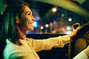 Profilo di donna felice che guida l'auto e si diverte durante il viaggio su strada di notte.