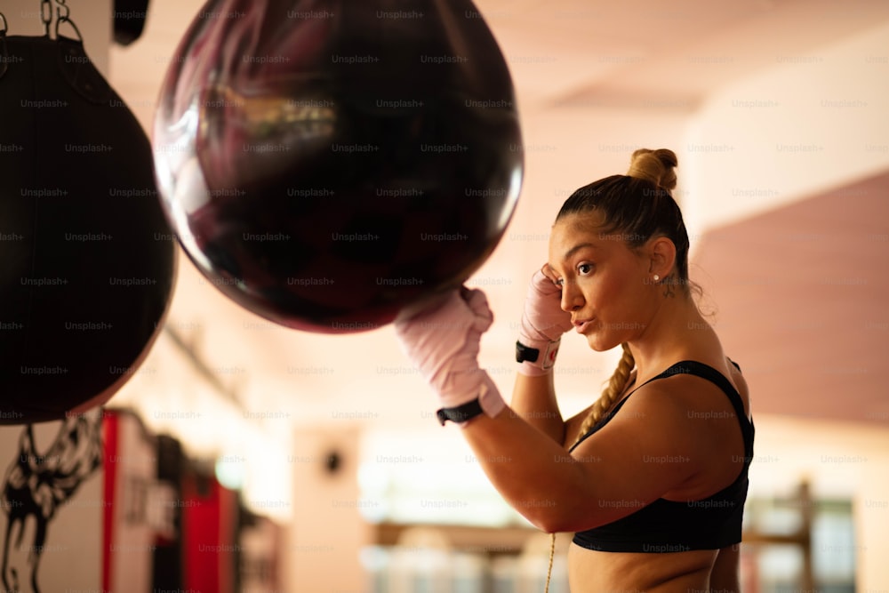 One woman, strong young lady, punching a  bag in gym alone. Focus is on woman.  alone. Focus is on woman.