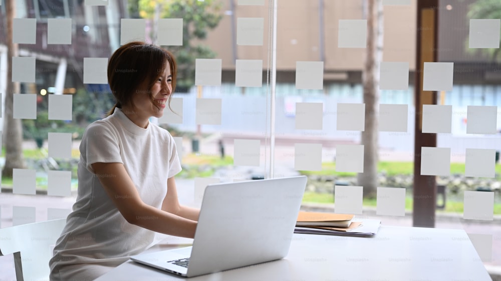 Heureuse femme d’affaires prospère souriant et travaillant sur un ordinateur portable dans un bureau moderne.